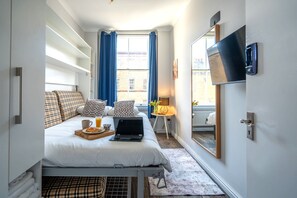 A hotel room with a bed, a laptop, breakfast tray, and a TV on the wall. - E2 Shoreditch House (London)