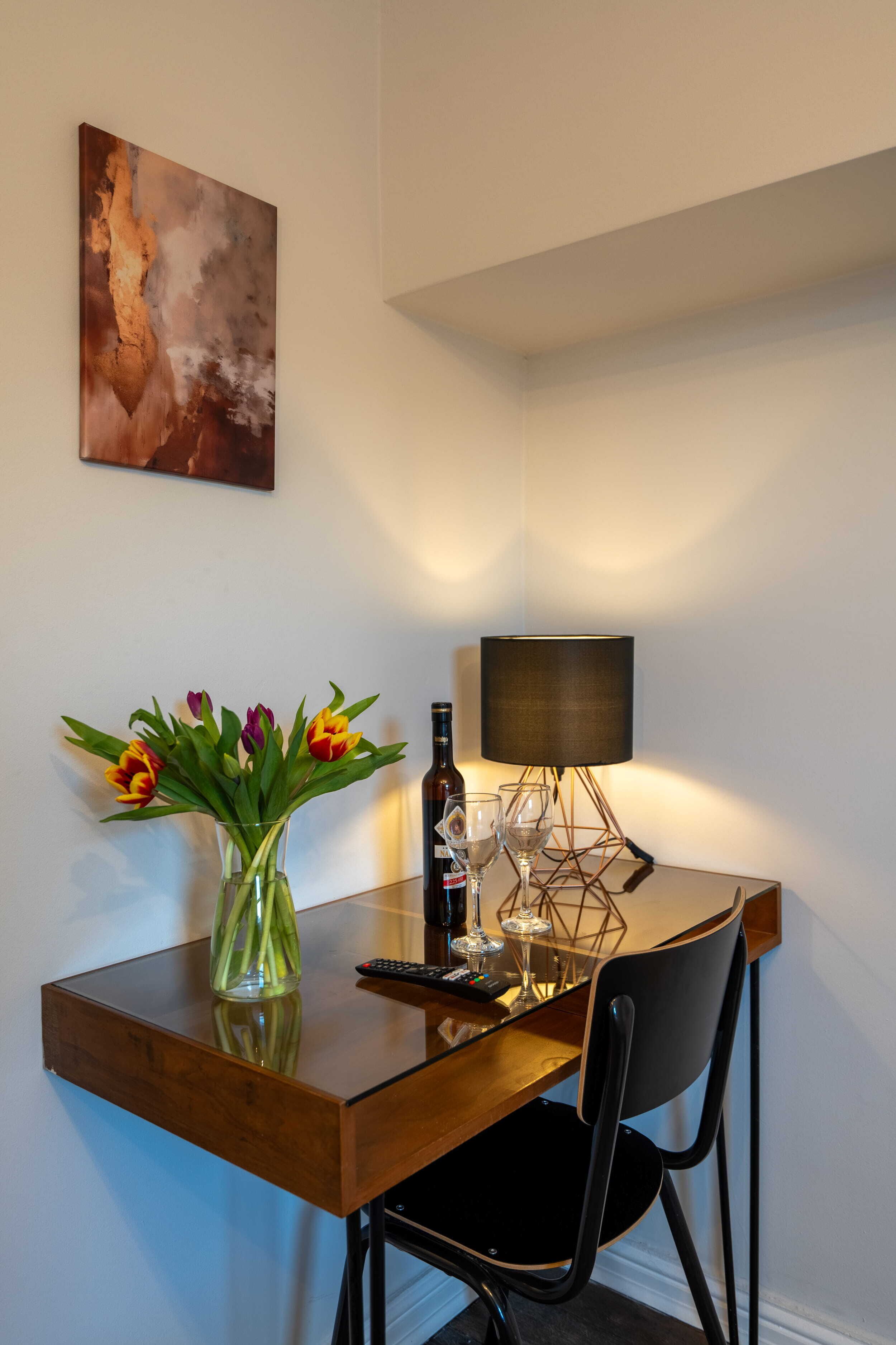 A dining table with a vase of flowers, a bottle of wine, and a lamp.