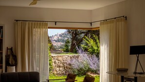 A room with a ceiling fan, a sofa, a table with a music stand, and a view of a hillside with buildings and trees. - Beautiful house on the edge of the charming village of Pigna (Pigna)