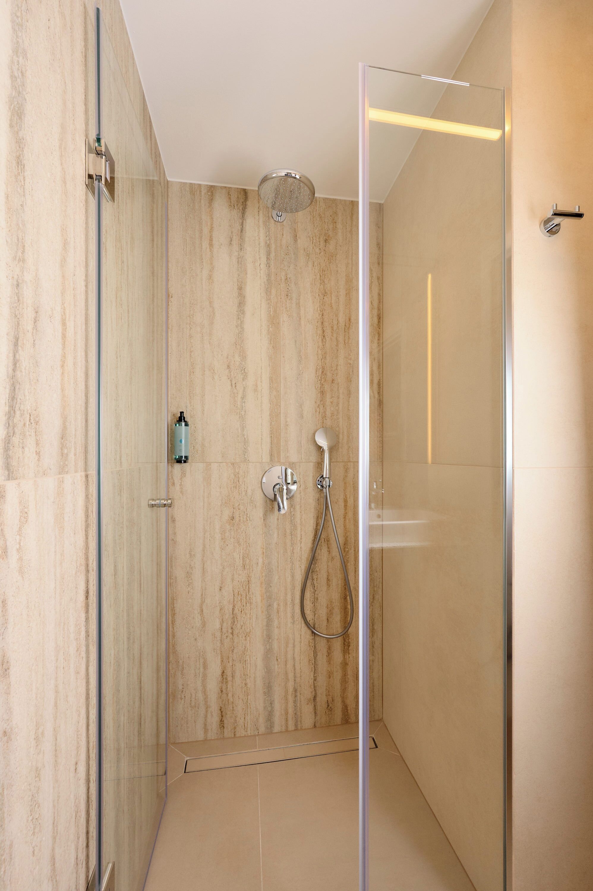A modern shower with a glass door, a handheld showerhead, and a wall-mounted control.