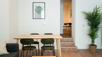 Una sala de estar moderna con una mesa de comedor de madera, sillas verdes, un sofá, una obra de arte enmarcada, una escalera que conduce a otra habitación y una planta en maceta.