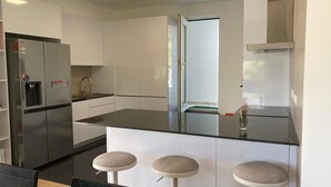 Una cocina moderna con un refrigerador de acero inoxidable, armarios blancos, una encimera negra y tres taburetes.