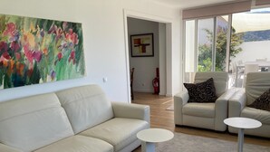 Una sala de estar con un sofá color beige, dos mesitas de noche blancas y un cuadro en la pared.
