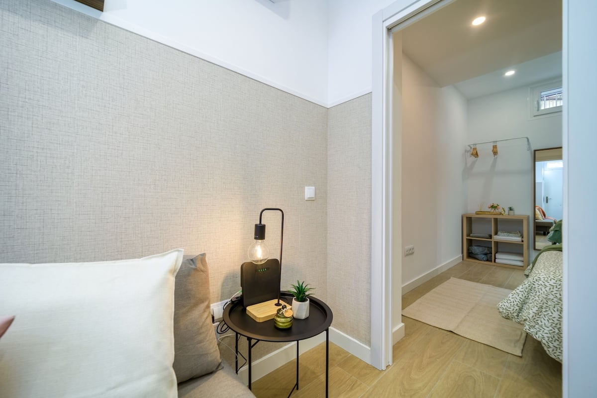 Un dormitorio moderno con una cama, una mesita de noche con lámpara, un espejo y un estante de madera con toallas.