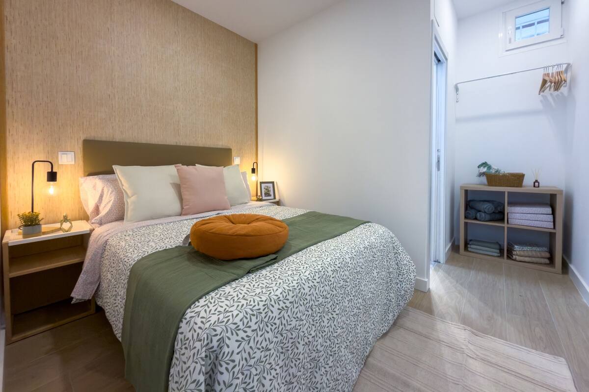 Un dormitorio moderno con cama, mesitas de noche, una estantería en la pared y un ventanal.