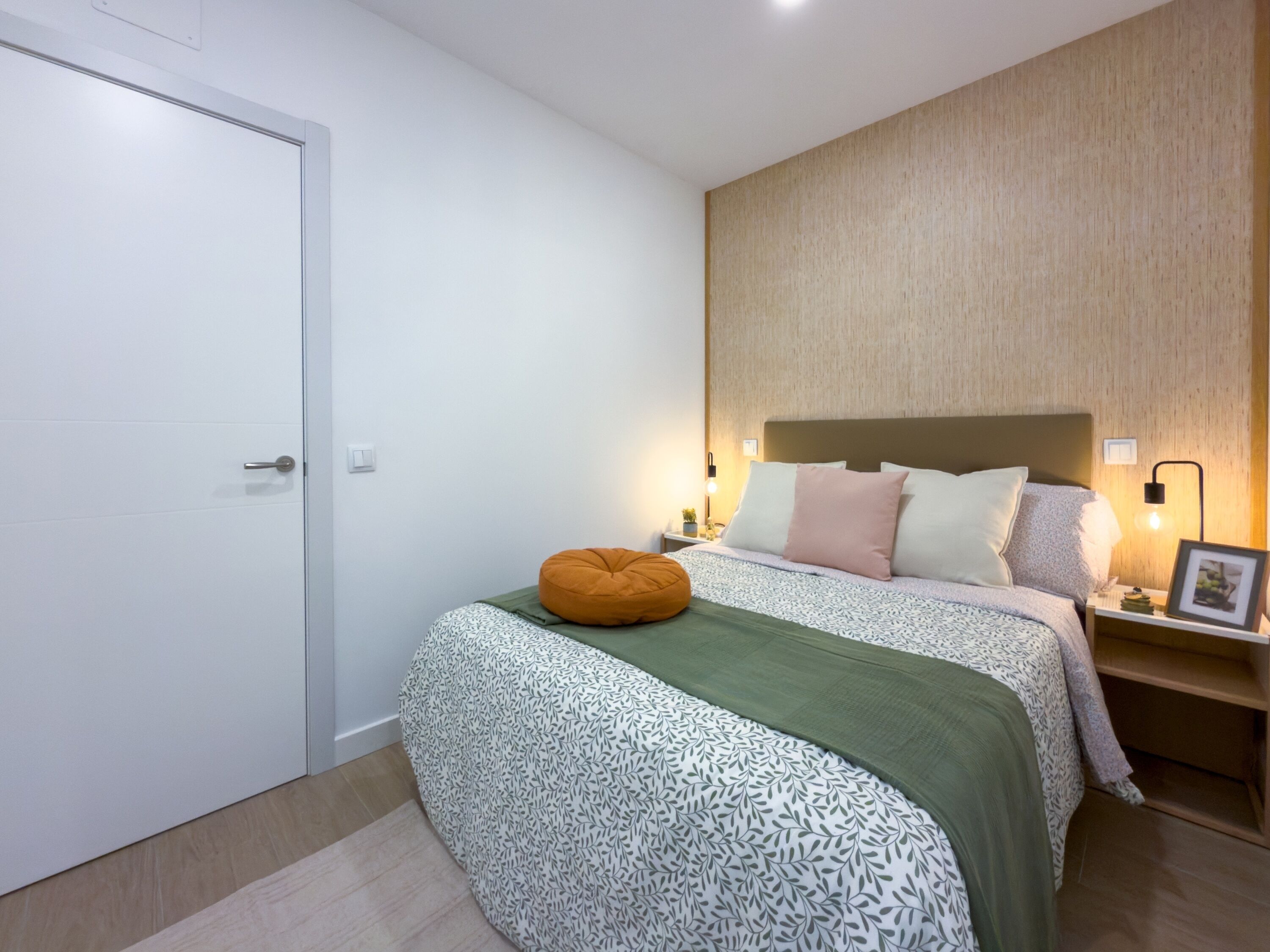A bedroom with a bed, a nightstand, a wall-mounted light, and a door.