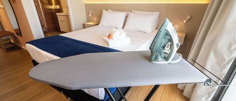 Una cama bien hecha con una manta azul, una tabla de planchar con un planchador y un piso de madera.