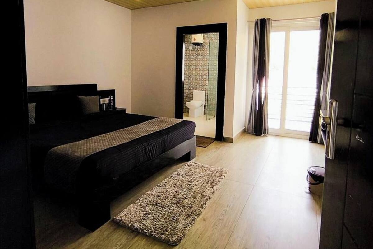 Ein Schlafzimmer mit Bett, Deckenventilator, Holzboden und Blick ins Badezimmer.