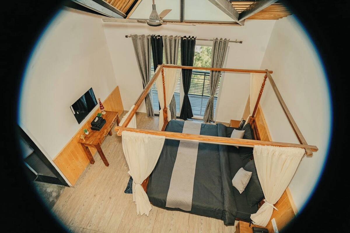 Ein Zimmer mit einem Bett, einem Fernseher, einem Holztisch und einem Fenster mit Vorhängen.