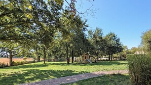 Un parco con un'area giochi, un sentiero sterrato e alberi.
