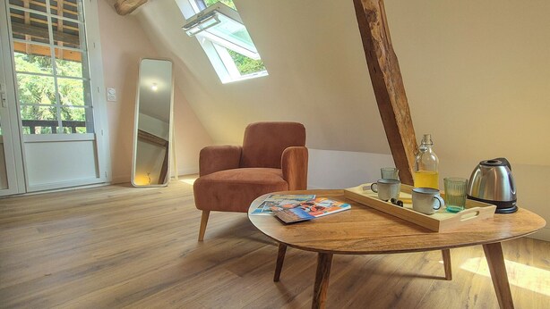 Una stanza con pavimento in legno, una poltrona marrone, un tavolo in legno con un vassoio, un bollitore e una bottiglia d'acqua.