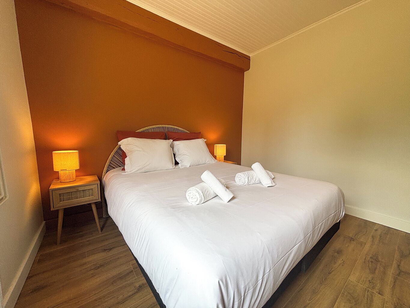 A hotel room with a large bed, two bedside lamps, and a wooden floor.