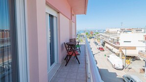 Ein Balkon mit Tisch und Stühlen, mit Blick auf eine Straße mit Gebäuden und einem klaren Himmel.
