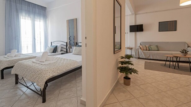 Ein modernes Hotelzimmer mit zwei Betten, einer Couch, einem Esstisch und einer Topfpflanze.