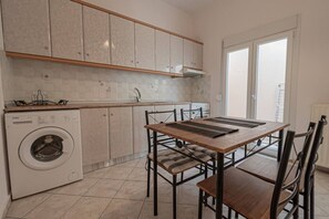 A kitchen with a washing machine, a table with chairs, and a window. - MelMare Sol Apartment by RentalsPro (Nea Moudania)