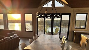 Un espace repas comprenant une grande table et des chaises, de grandes fenêtres donnant sur un plan d’eau et un plafond en bois.
