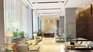 A modern hotel lobby with a sofa area, a reception desk, and a bed with a metal frame. - Pattaya Studio Walk to Beach Walking Street (Pattaya)