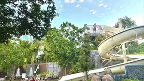 A pool with a water slide, lounge chairs, and a rocky landscape. - Pattaya Studio Walk to Beach Walking Street (Pattaya)