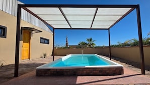 A rectangular pool with a white interior and a brick base, surrounded by a pergola with a white canopy, set against a building with a yellow door and a clear blue sky. - The Big House Baja - 5BR Vacation Rental with Private Pool (San Felipe)