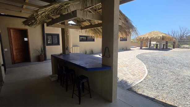 A covered outdoor bar area with stools, a thatched roof structure, and a paved courtyard. - The Big House Baja - 5BR Vacation Rental with Private Pool (San Felipe)