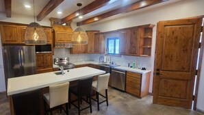 A kitchen with wooden cabinets, a central island, pendant lights, and a stone accent wall. - The Big House Baja - 5BR Vacation Rental with Private Pool (San Felipe)