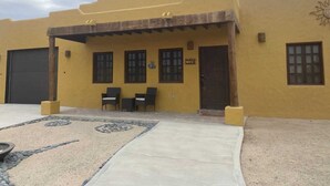 A yellow building with a covered patio, two windows, and a door. - Casa Serenidad | Pete's Camp | Baja 250 Rental | Sleeps 5 (San Felipe)