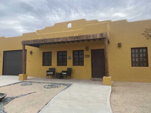 A yellow building with a covered patio, two windows, and a door. - Casa Serenidad | Pete's Camp | Baja 250 Rental | Sleeps 5 (San Felipe)