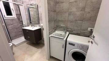 Un baño pequeño con ducha, lavabo, espejo, armario y lavadora.