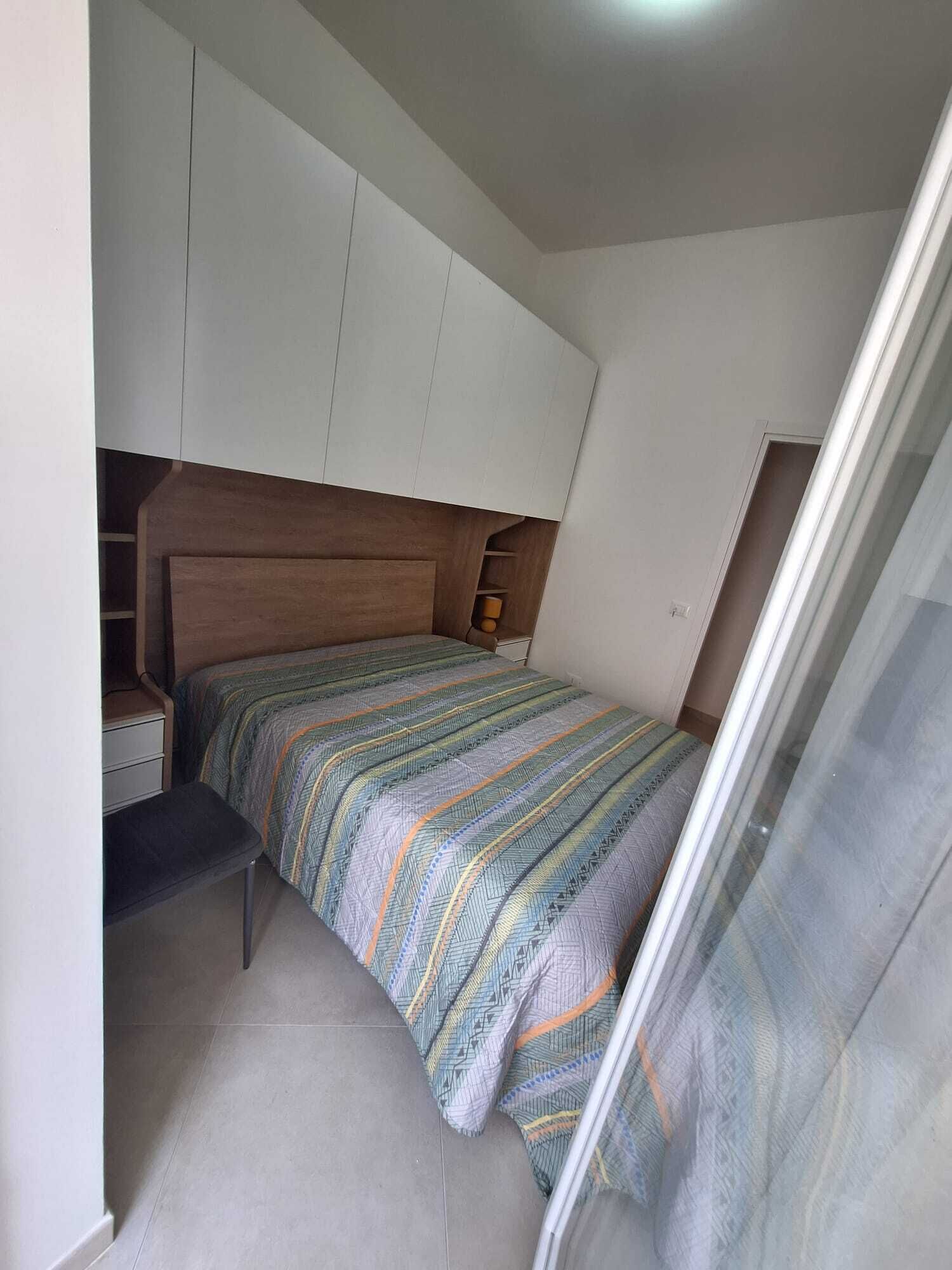 A small, compact bedroom with a bed, a nightstand, a bench, and a wardrobe.