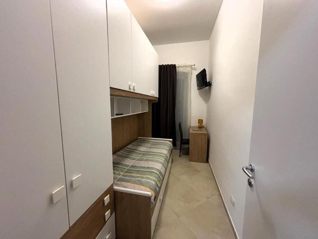 Una habitación pequeña y estrecha con una cama, un televisor en la pared y una puerta.