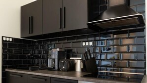 Een moderne keuken met zwarte kastjes, een roestvrijstalen afzuigkap en een zwart betegelde achterwand.