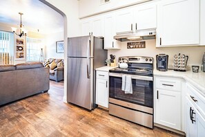 Una cocina moderna con electrodomésticos de acero inoxidable, armarios blancos y una zona de estar acogedora con sofá y cojines.