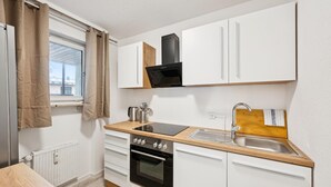 A compact kitchen with a stove, oven, sink, and a window with curtains.