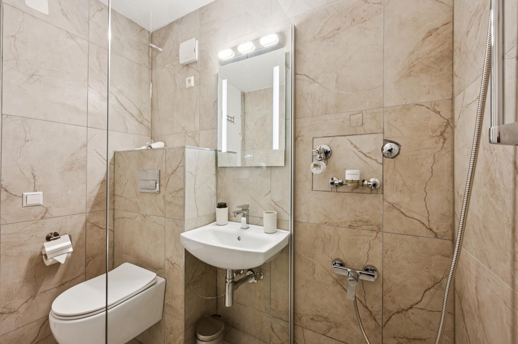 Ein modernes Badezimmer mit Toilette, Waschbecken, Spiegel und Dusche.