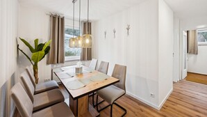A modern dining area with a wooden table, cushioned chairs, a hanging light fixture, and a potted plant.