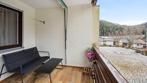 A balcony with a black bench, a potted plant, and a view of a snowy landscape and houses.