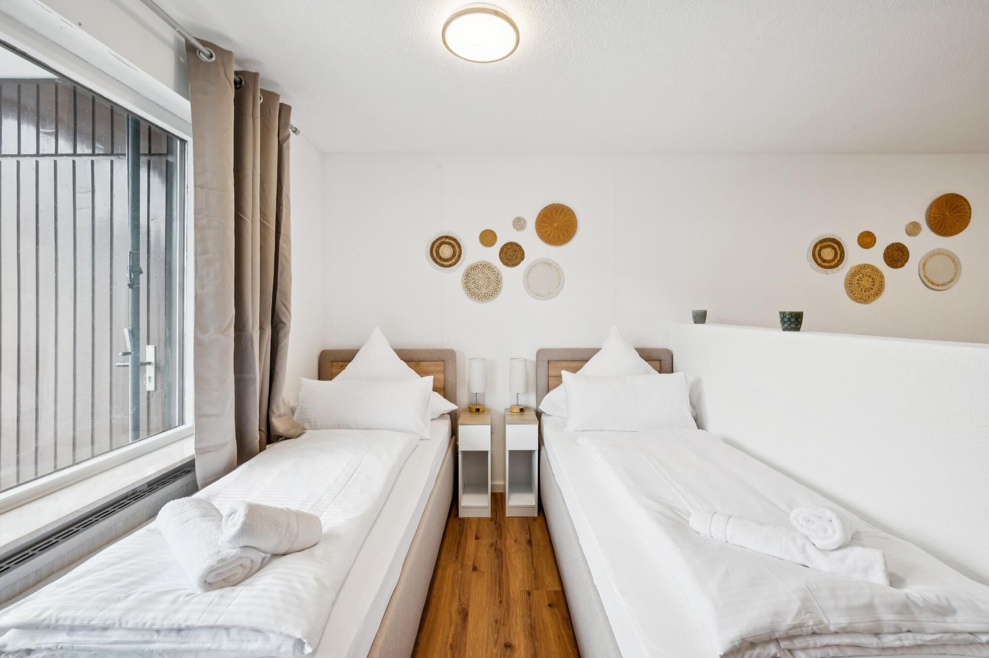 Una habitación de hotel con dos camas, una ventana con cortinas, una lámpara en el techo y decoración en las paredes.