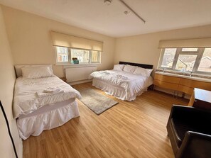 Ein Schlafzimmer mit zwei Betten, einem Schreibtisch, einem Stuhl und großen Fenstern.