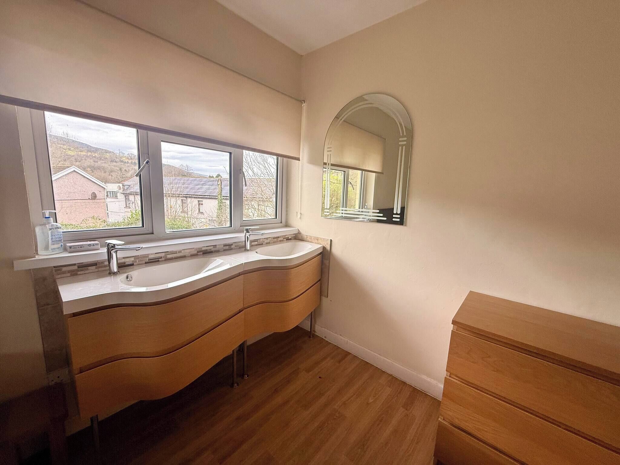 A bathroom with a double vanity, a large mirror, and a window with a view of buildings.