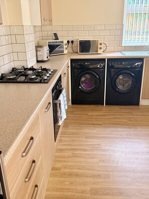 Uma cozinha moderna com fogão a gás, micro-ondas e duas máquinas de lavar roupa.