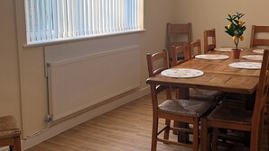 Een eethoek met een houten tafel, stoelen, een potplant en een raam met jaloezieën.
