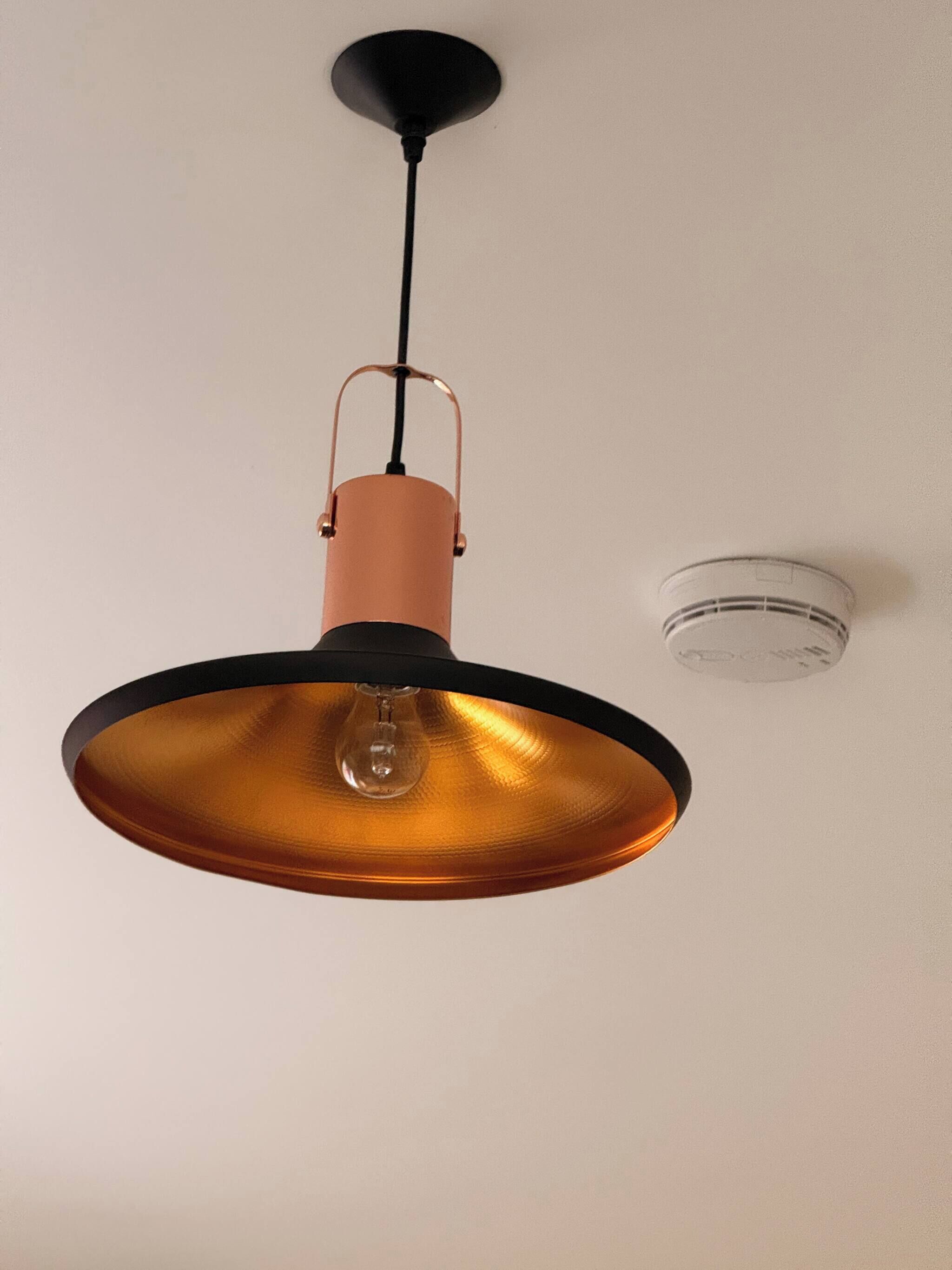 A pendant light fixture with a copper-colored shade and a black cord.
