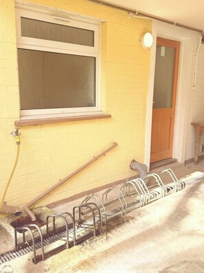 Un edificio amarillo con una ventana, una puerta y un aparcamiento para bicicletas de metal afuera.