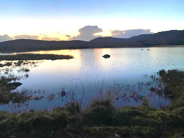 A calm lake with a small island, surrounded by hills and sparse vegetation.