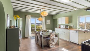 Una cucina con zona pranzo, pavimento in legno, vista attraverso una porta in vetro e un lampadario.