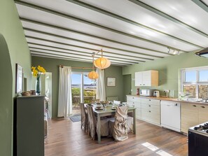 A kitchen with a dining area, wooden flooring, a view through a glass door, and a hanging light fixture. - Bun Inbhir cottage with views (Rosmuck)
