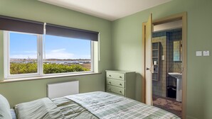 Una camera da letto con un letto, una cassettiera, una finestra con vista e un bagno visibile attraverso una porta aperta.