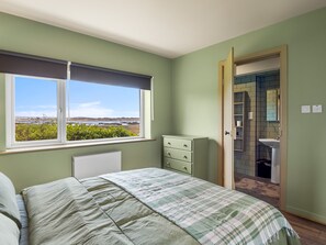 A bedroom with a bed, a dresser, a window with a view, and a bathroom visible through an open door. - Bun Inbhir cottage with views (Rosmuck)