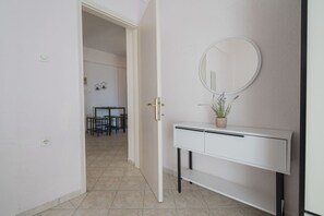 A hallway with a white console table, a round mirror, and a potted plant. - MelMare Azuro Apartment by RentalsPro (Nea Moudania)