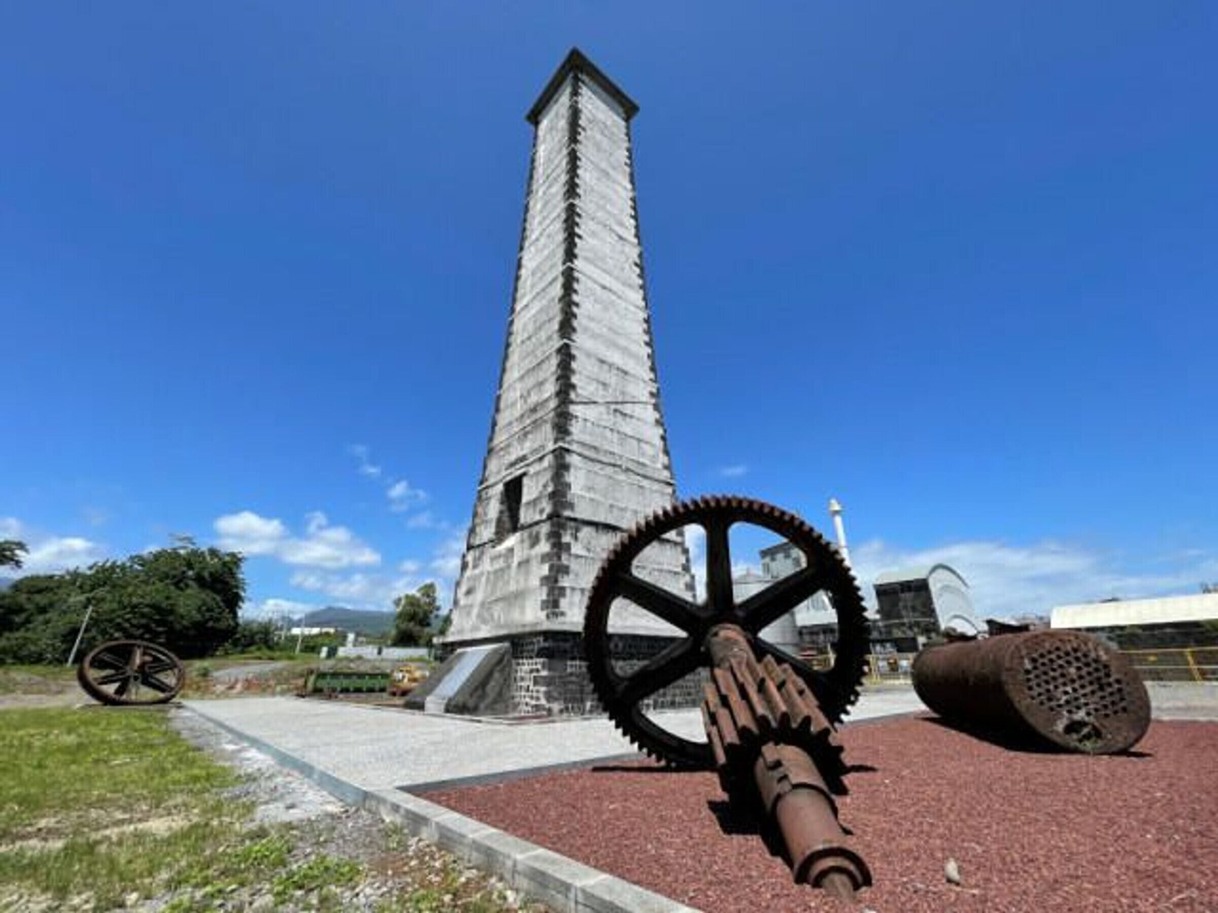A tall monument with a gear and a cylindrical object in front.